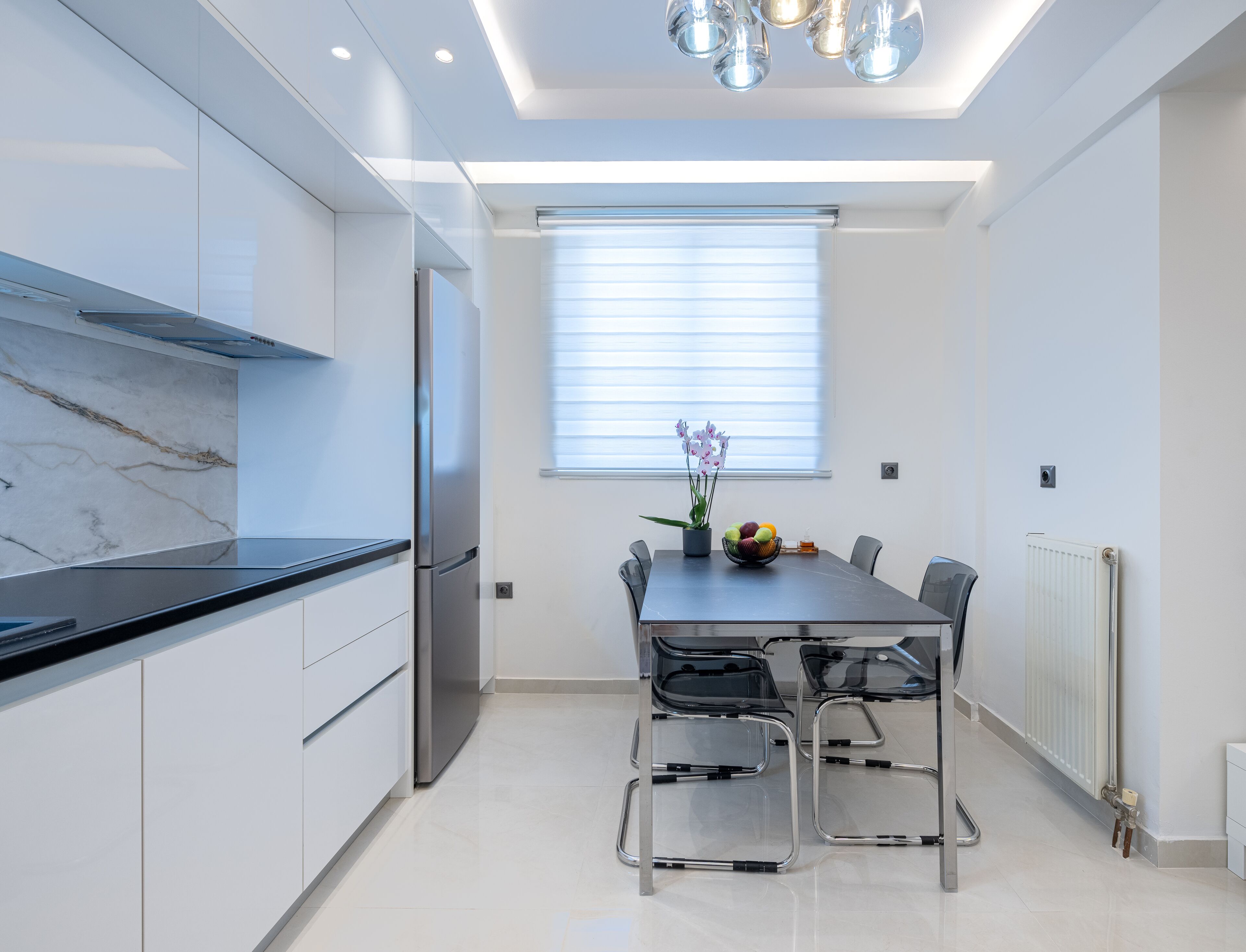 Une cuisine moderne dotée d’un pare-feu en marbre, d’appareils électroménagers en acier inoxydable et d’un coin repas avec une table et des chaises.