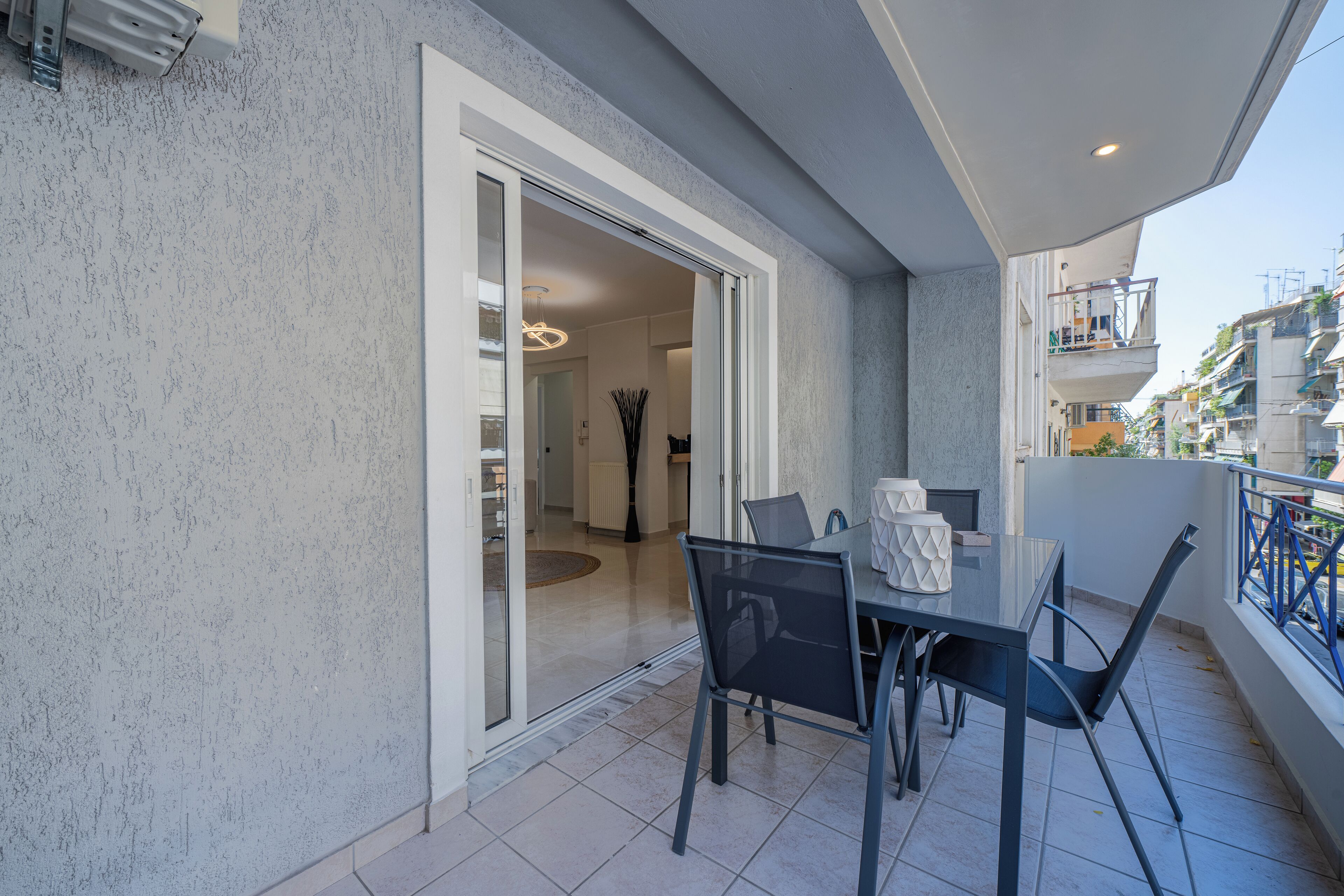 A balcony with a table and chairs, a sliding glass door leading to an interior space, and a view of the cityscape.