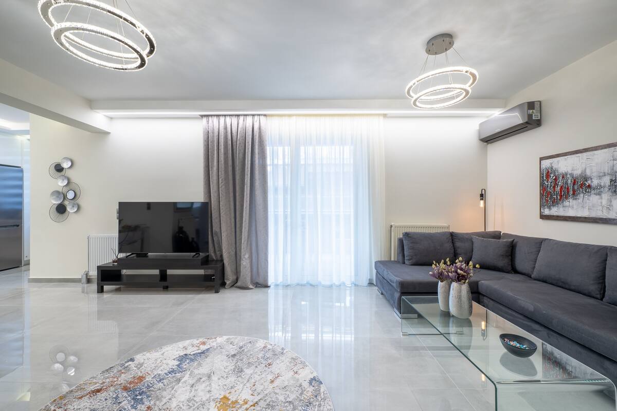 A modern living room with a grey sofa, a glass coffee table, and a TV.