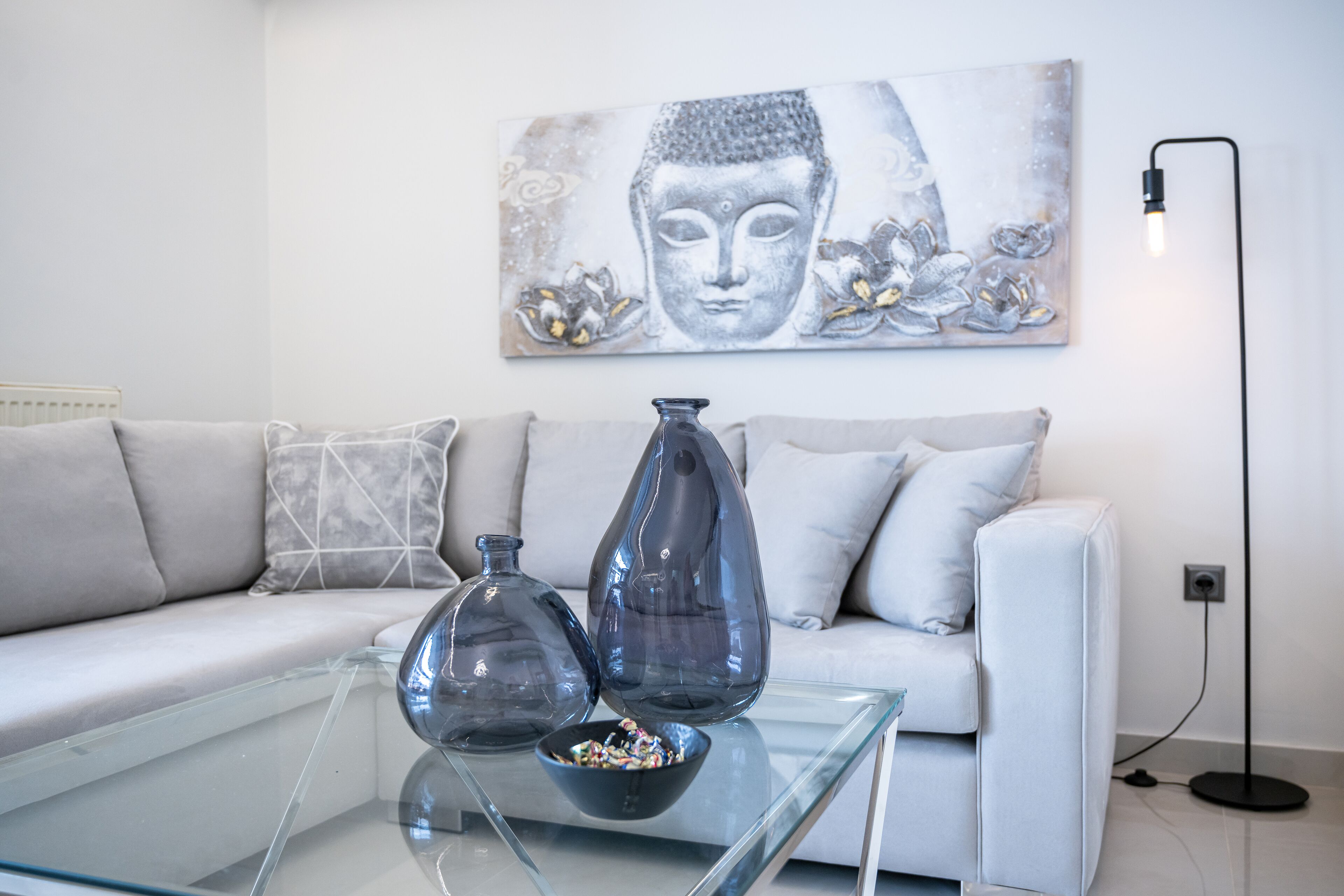 Ein modernes Wohnzimmer mit einem Glastisch, zwei dekorativen Vasen und einem Buddha-Gemälde an der Wand.