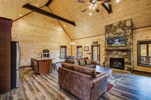 A spacious living area with a stone fireplace, wooden ceiling, and a large TV mounted above it.