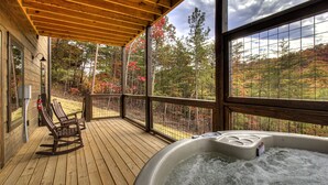 Eine Holzterrasse mit Whirlpool und Schaukelstühlen, mit Blick auf ein bewaldetes Gebiet.