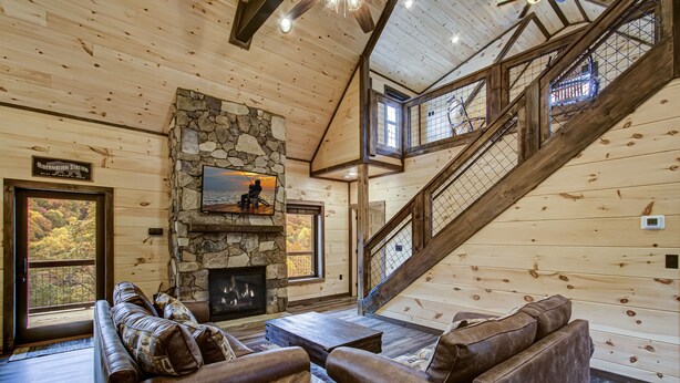Ein Holzblockhaus-Interieur mit Kamin aus Stein, einem großen Sofa und einer Treppe.