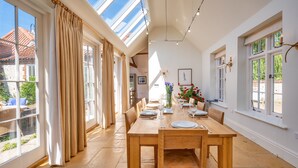 A spacious dining area with a wooden table set for six, large windows with curtains, and a skylight. - School House, Burnham Thorpe, Norfolk (Burnham Thorpe)