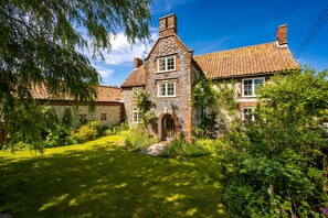 A traditional stone house with a well-maintained garden and a clear blue sky.