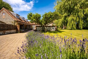 A stone building with a tiled roof, a covered patio, and a garden with lavender.