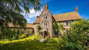 A stone building with a tiled roof, a central entrance, and a well-maintained garden. - School House, Burnham Thorpe, Norfolk (Burnham Thorpe)