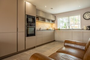 A modern kitchen with built-in appliances, a large window, and a brown leather sofa.