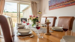 Mesa de jantar posta para quatro pessoas, com taças de vinho, pratos e um centro de mesa com velas.