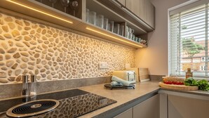 Cozinha moderna com painel de pedra, fogão embutido e janela com persianas.
