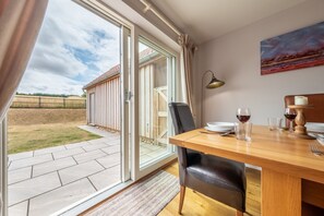 A dining area with a table set for two, a sliding glass door leading to a patio, and a painting on the wall. - Field View, Sedgeford, Norfolk (Sedgeford)
