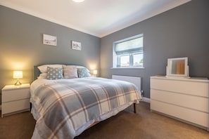 Quarto com cama, mesas de cabeceira, penteadeira e janela.
