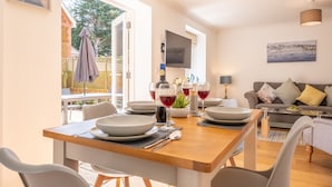 Un coin repas avec une table en bois dressée pour quatre personnes, un canapé et un téléviseur fixé au mur.