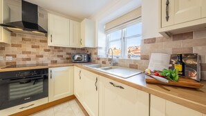 Une cuisine moderne avec des meubles blancs, un four Bosch, un micro-ondes et un plan de travail en bois agrémenté d’une planche à découper et de produits frais.