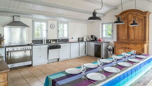 Een keuken met een lange eettafel gedekt voor een maaltijd, een fornuis en een vaatwasser.
