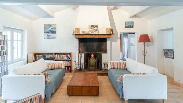 Een ruime woonkamer met twee witte banken, een houten salontafel en een open haard. Er staan boekenkasten en een lamp in de kamer.