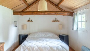 Een slaapkamer met een houten plafond, een bed met een witte sprei, twee nachtkastjes met lampen en een raam met gordijnen.