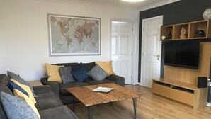 Una sala de estar con un sofá seccional, una mesa de centro de madera, un televisor de pantalla plana y un mapa mundial en la pared.