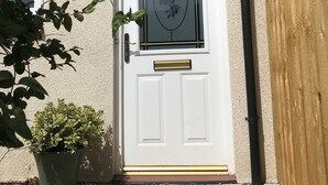 Una puerta principal blanca con un panel de vidrio, una pequeña planta en maceta y un buzón.