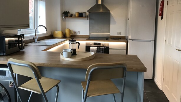 Una cocina moderna con una isla central, dos sillas, una cafetera y un refrigerador.