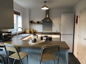 Eine moderne Küche mit einer zentralen Kochinsel, zwei Stühlen, einer Kaffeemaschine und einem Kühlschrank.