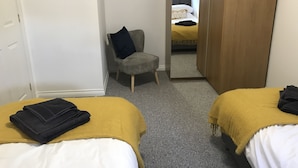 Habitación de hotel con dos camas, una silla, un armario y un espejo que refleja otra habitación.