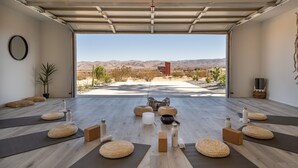 Une pièce spacieuse avec une grande porte ouverte donnant sur un paysage désertique, comprenant des tapis de yoga, des coussins et un espace dédié à la méditation.