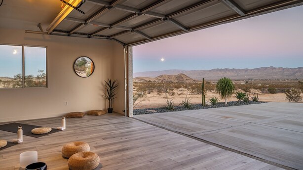 Une pièce spacieuse dotée d’un grand plancher en bois, d’un tapis de yoga, d’un coussin de méditation et offrant une vue sur un paysage désertique.