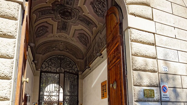 An arched entrance with a wooden door and a metal gate, leading to a building with stone walls and a tiled floor. - Villa Royal B&B (Florence)