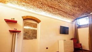 A room with a stone wall, a TV mounted on the wall, a radiator, a red chair, and a white dresser. - Villa Royal B&B (Florence)