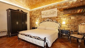 A bedroom with a stone wall, a large bed, a wardrobe, and a chair. - Villa Royal B&B (Florence)