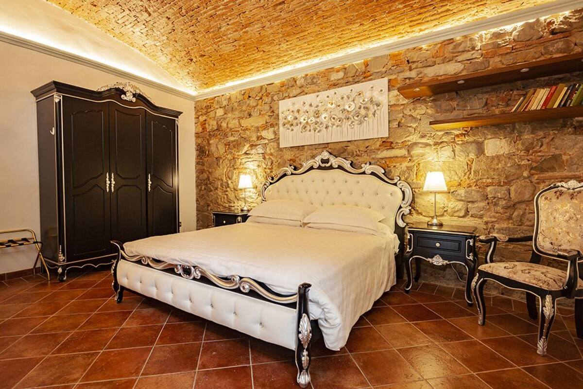 A bedroom with a stone wall, a large bed, a wardrobe, and a chair.