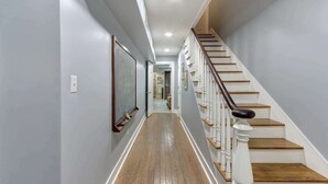 Ein Korridor mit Holzboden, weißer Wand und einer Treppe mit weißen Geländern und Holzstufen.