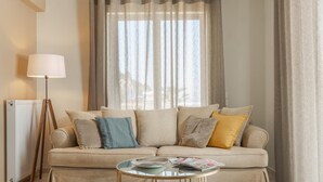 Un soggiorno con un divano beige, un tavolino in vetro, una lampada da terra e una finestra con tende leggere.