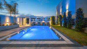 Une piscine avec des chaises longues, un bâtiment bien éclairé et un ciel dégagé.