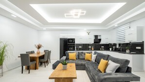 Un salon moderne comprenant un coin repas, un canapé d’angle gris et une table basse en bois.