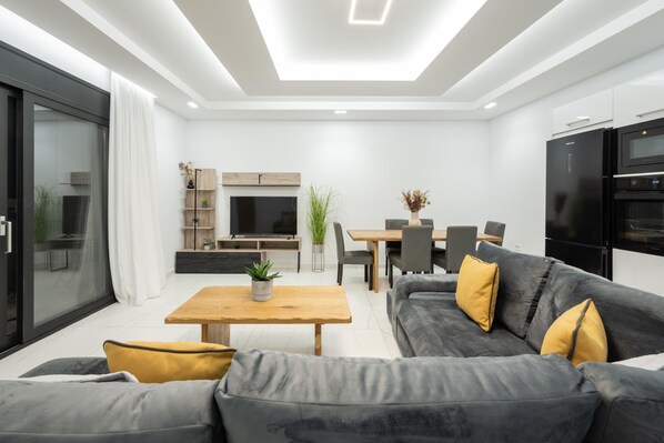 A modern living room with a sofa, coffee table, TV, and dining area.