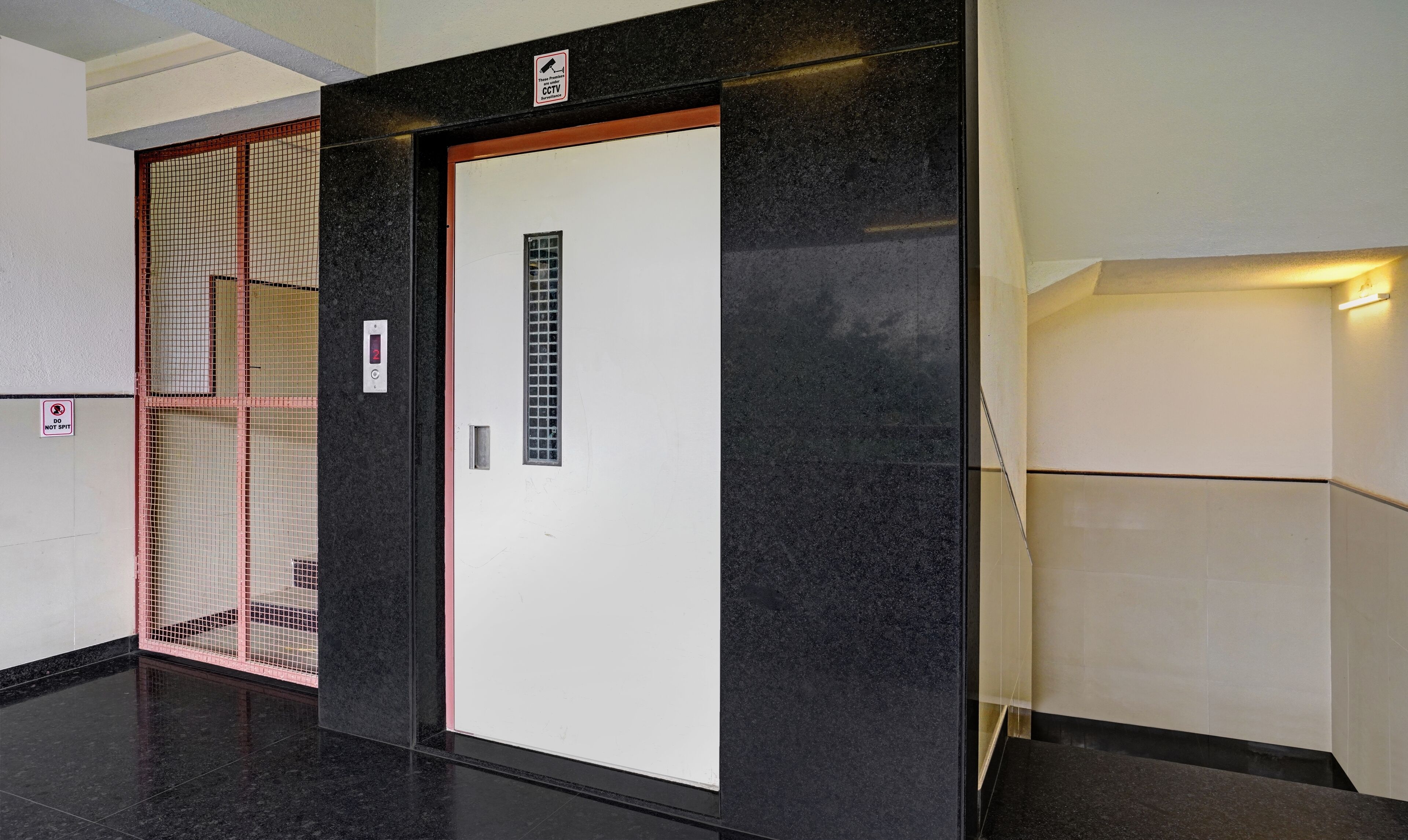 An elevator with a digital display, a "DO NOT SPIT" sign, and a "CCTV" sign.