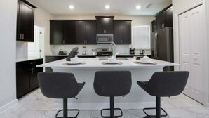 Une cuisine moderne avec des meubles de couleur sombre, un îlot central doté de tabourets et des appareils électroménagers intégrés.