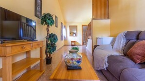 A living room with a TV on a wooden stand, a plant, a vase with colorful items, a couch, and a staircase leading to another room. - Antonella by Interhome (Deltebre)