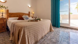 A bedroom with a wooden bed, a nightstand with a lamp, a bedside table with two glasses, and a view of the outdoors through a sliding door. - Antonella by Interhome (Deltebre)