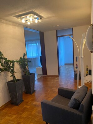 A spacious living room with a wooden floor, a grey sofa, and two large potted plants. - Nicely furnished apartment with parking space (Reutlingen)