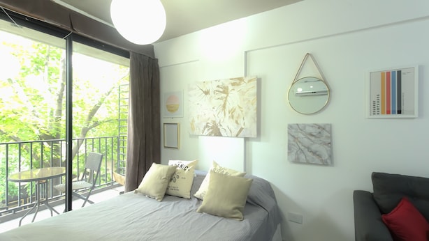 Un dormitorio con una cama, un espejo redondo, un cuadro enmarco y un balcón con mesa y sillas.