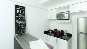Una cocina moderna con armarios blancos, un refrigerador de acero inoxidable, un microondas y una cafetera. Un letrero negro con letras blancas está montado en la pared.