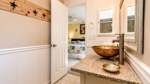 A bathroom with a wooden wall-mounted shelf, a large mirror, a granite countertop, and a wooden bowl sink. - Pet Friendly! Huge Heated Pool Quiet Neighborhood Close to Beach Gr8 4 Families! (Sebastian)