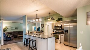 A modern kitchen with a central island, stainless steel appliances, and a dining area with a sofa and coffee table. - Pet Friendly! Huge Heated Pool Quiet Neighborhood Close to Beach Gr8 4 Families! (Sebastian)