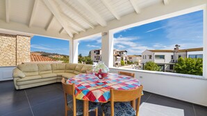 A sunlit patio with a round table, beige sofa, and a view of neighboring buildings. - Arbatax Sa Omu Bianca (Tortoli)