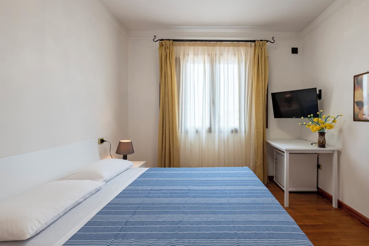 Une chambre d’hôtel avec un lit, un bureau, une télévision et une fenêtre avec des rideaux.