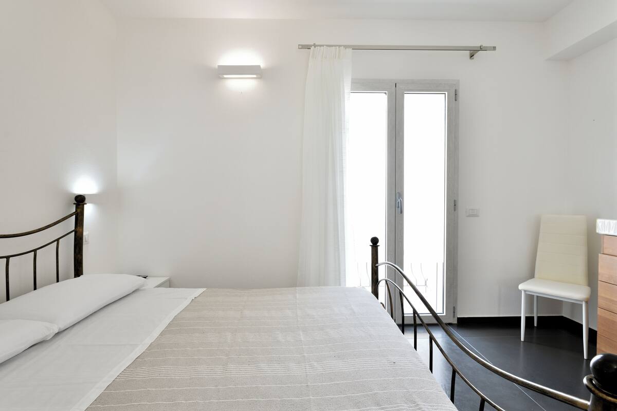 Une chambre à coucher avec un lit, une chaise, une commode et une fenêtre avec des rideaux.