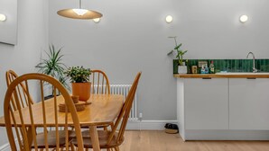 A modern kitchen with a wooden dining table and chairs, a built-in island with a sink, and pendant lighting. - Charming cottage in the Heart of Whitstable - Pass the Keys (Whitstable)